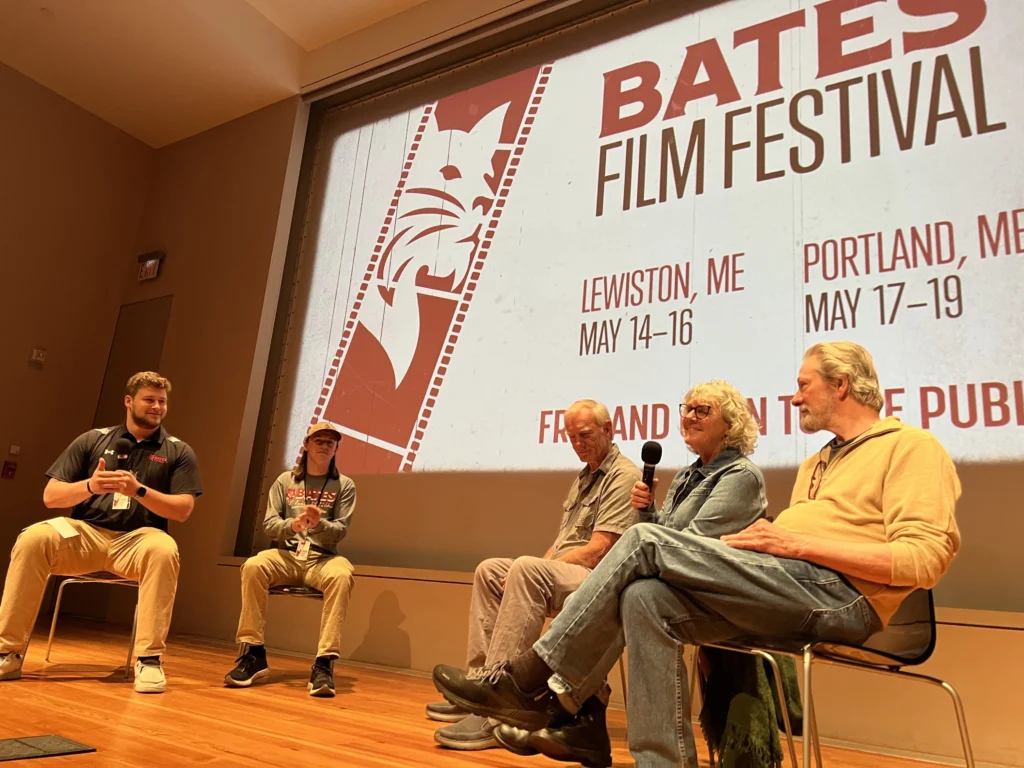 Five people sit on stage in front of a large screen displaying 